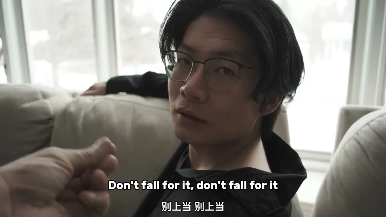 A young man in glasses looks into the camera from a sofa, with the subtitle "Don't fall for it, don't fall for it" in English and Chinese