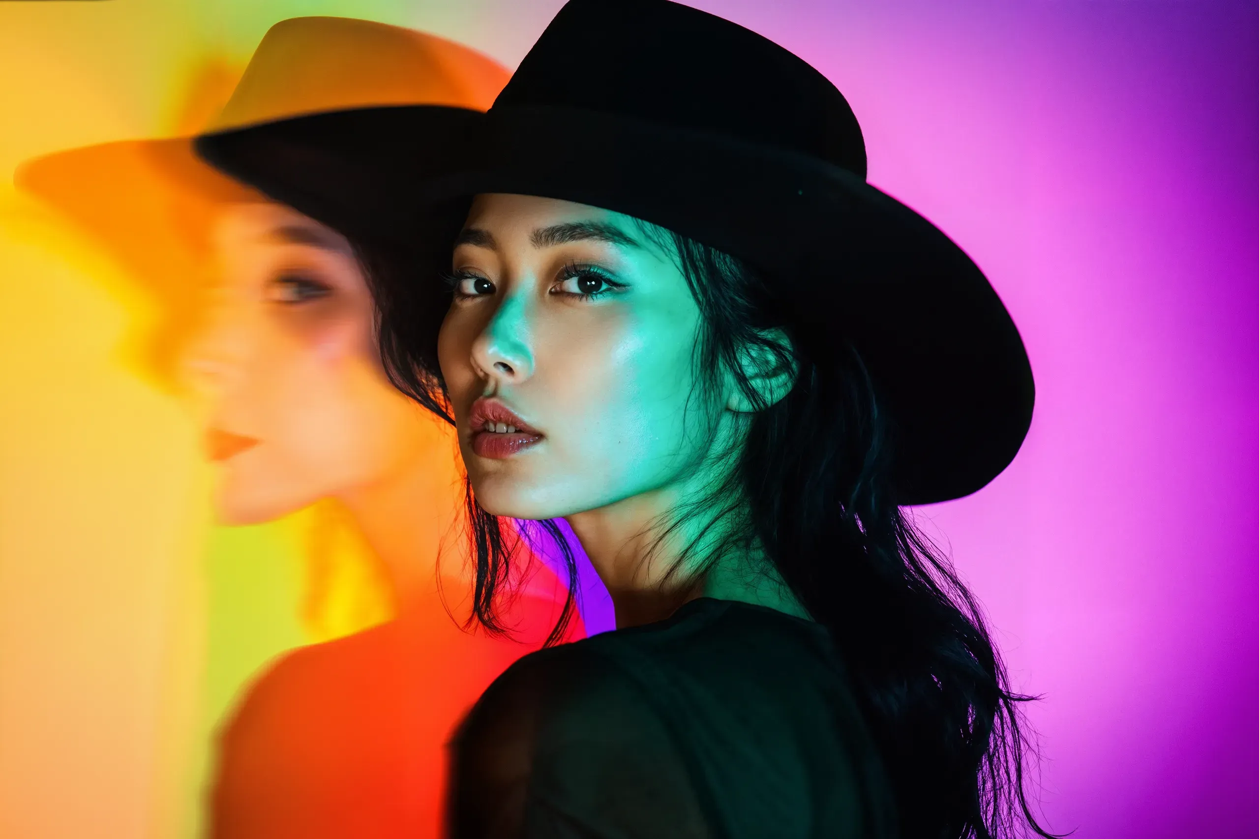 AI-generated portrait of a woman in a black wide-brimmed hat lit in green, with a blurred double of her face against orange and magenta light