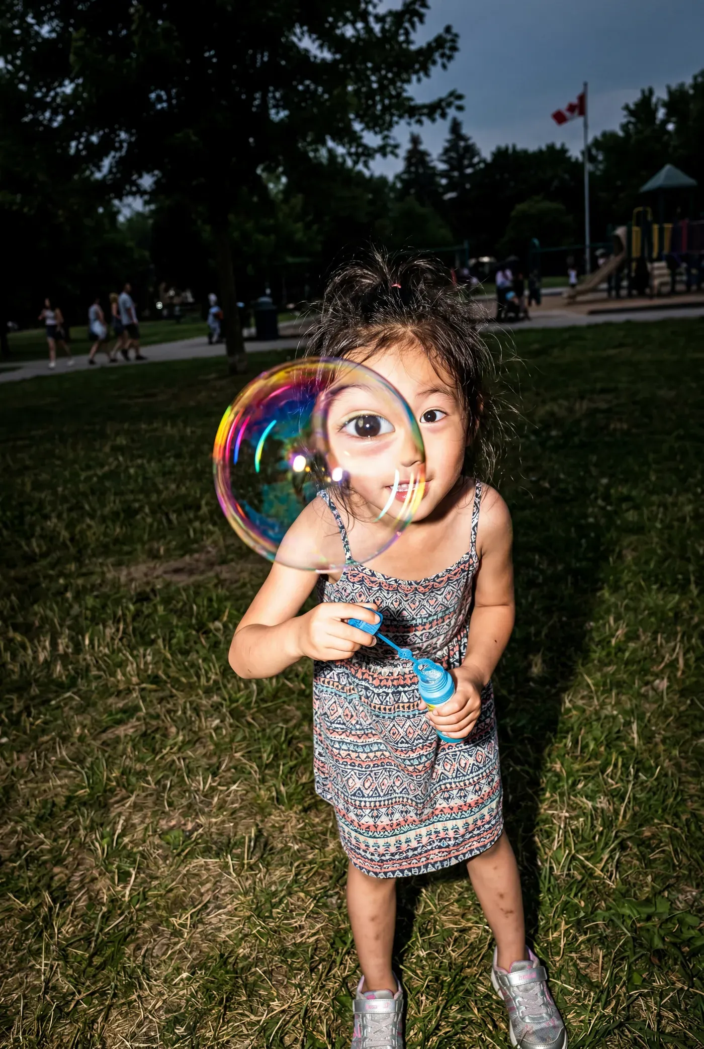 AI-generated street photo of a small girl in a park blowing a soap bubble that sits over one eye like a giant lens
