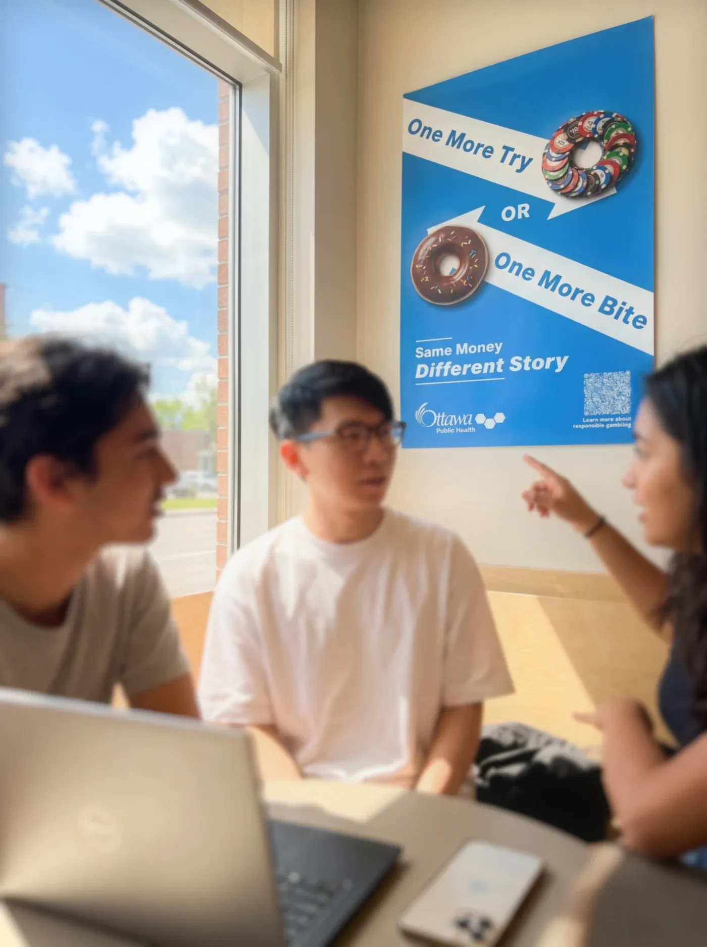 The redesigned blue poster on a café wall above three people talking at a table with a laptop