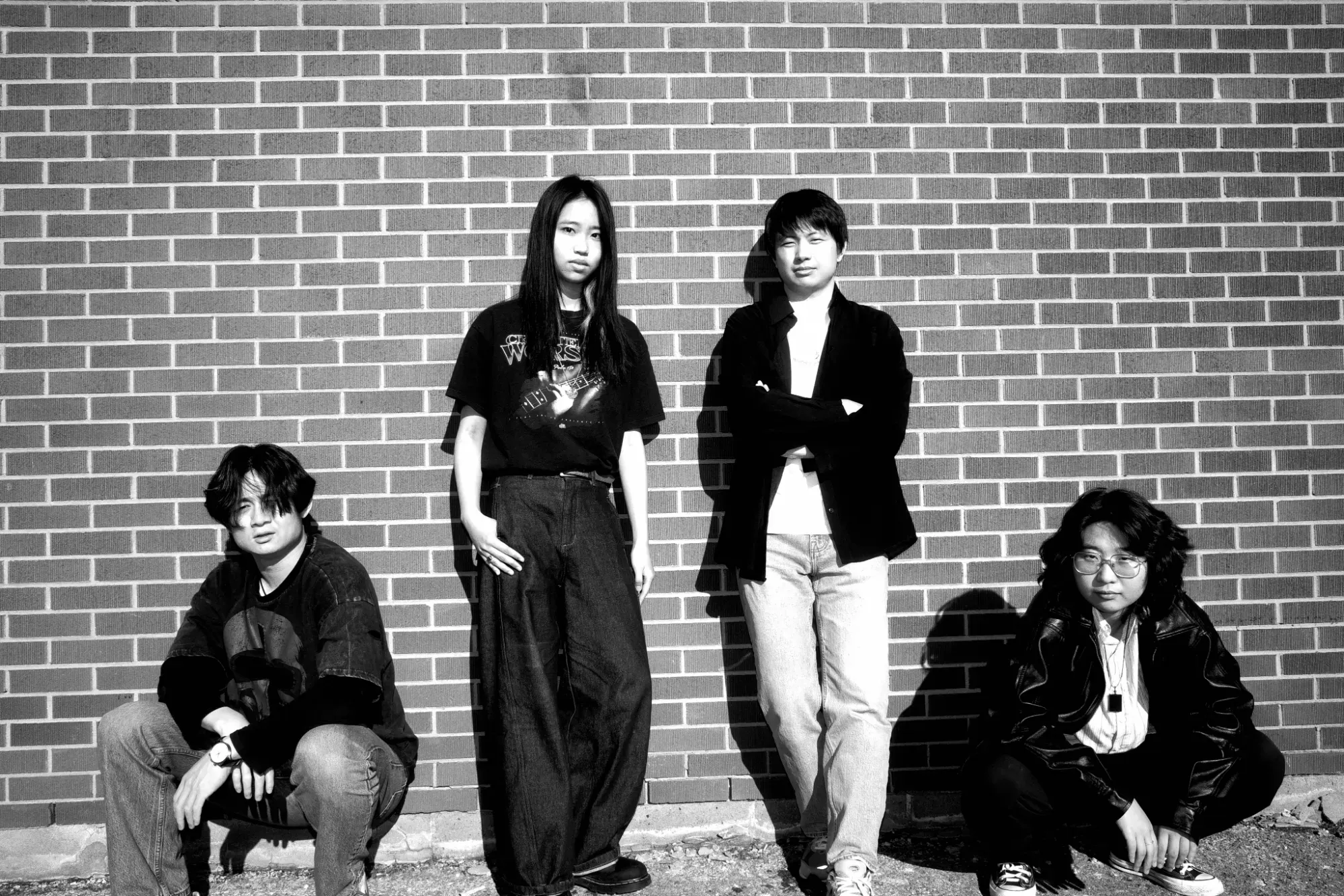 The four band members in black and white against a brick wall, two standing and two crouching
