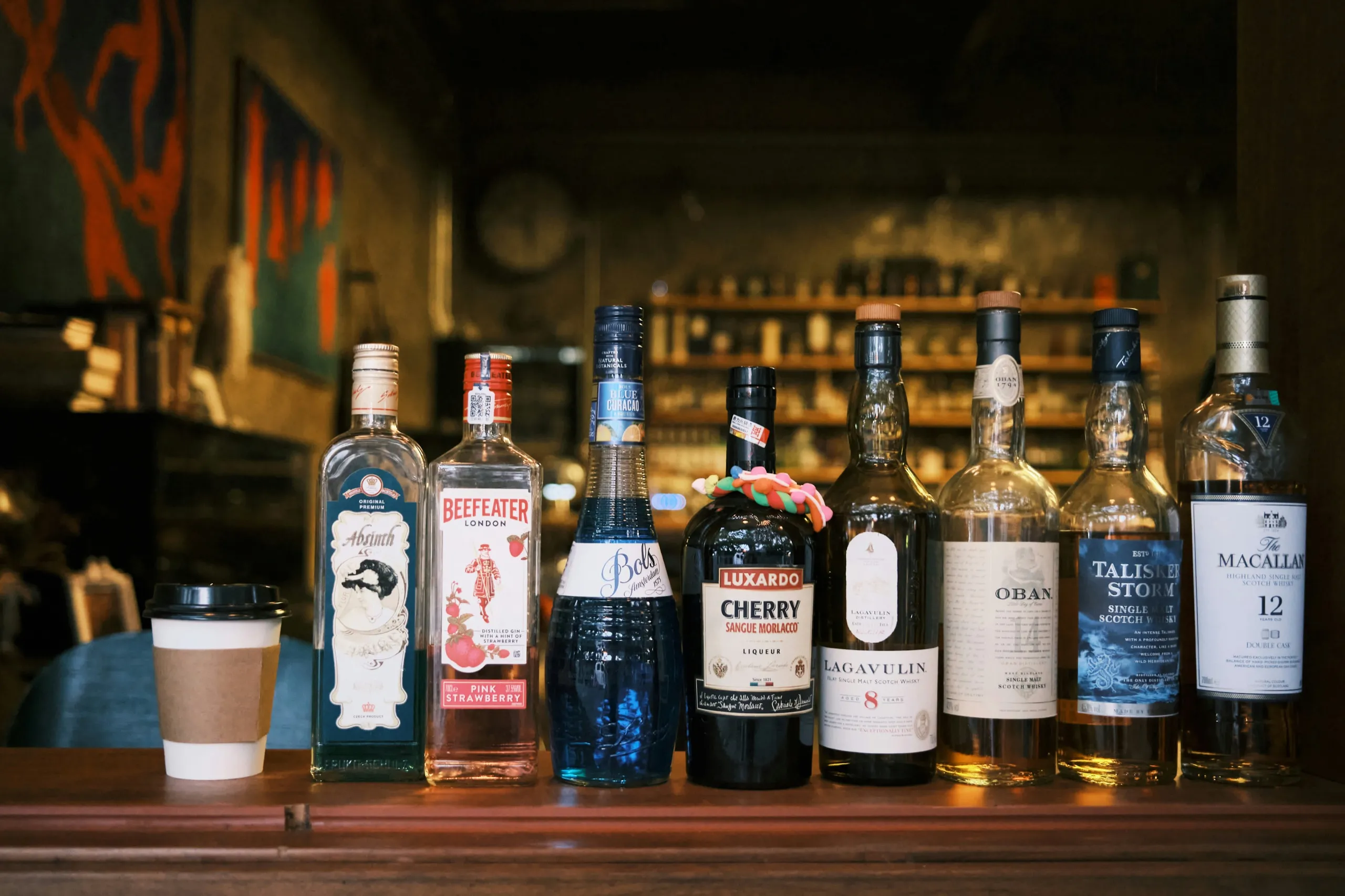 A row of liquor bottles and a paper coffee cup lined up on a bar counter