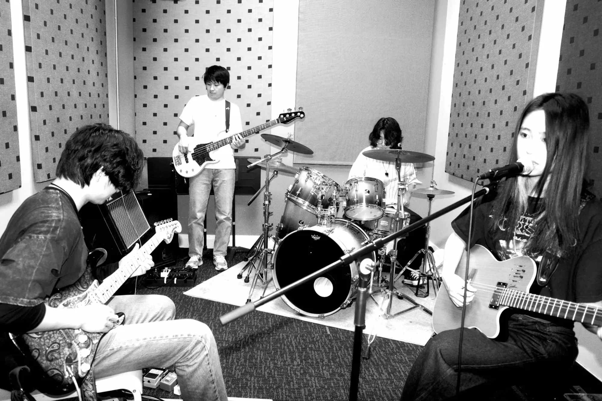 The band rehearsing in a small room with acoustic panels: guitar, bass, drums and the vocalist at a microphone