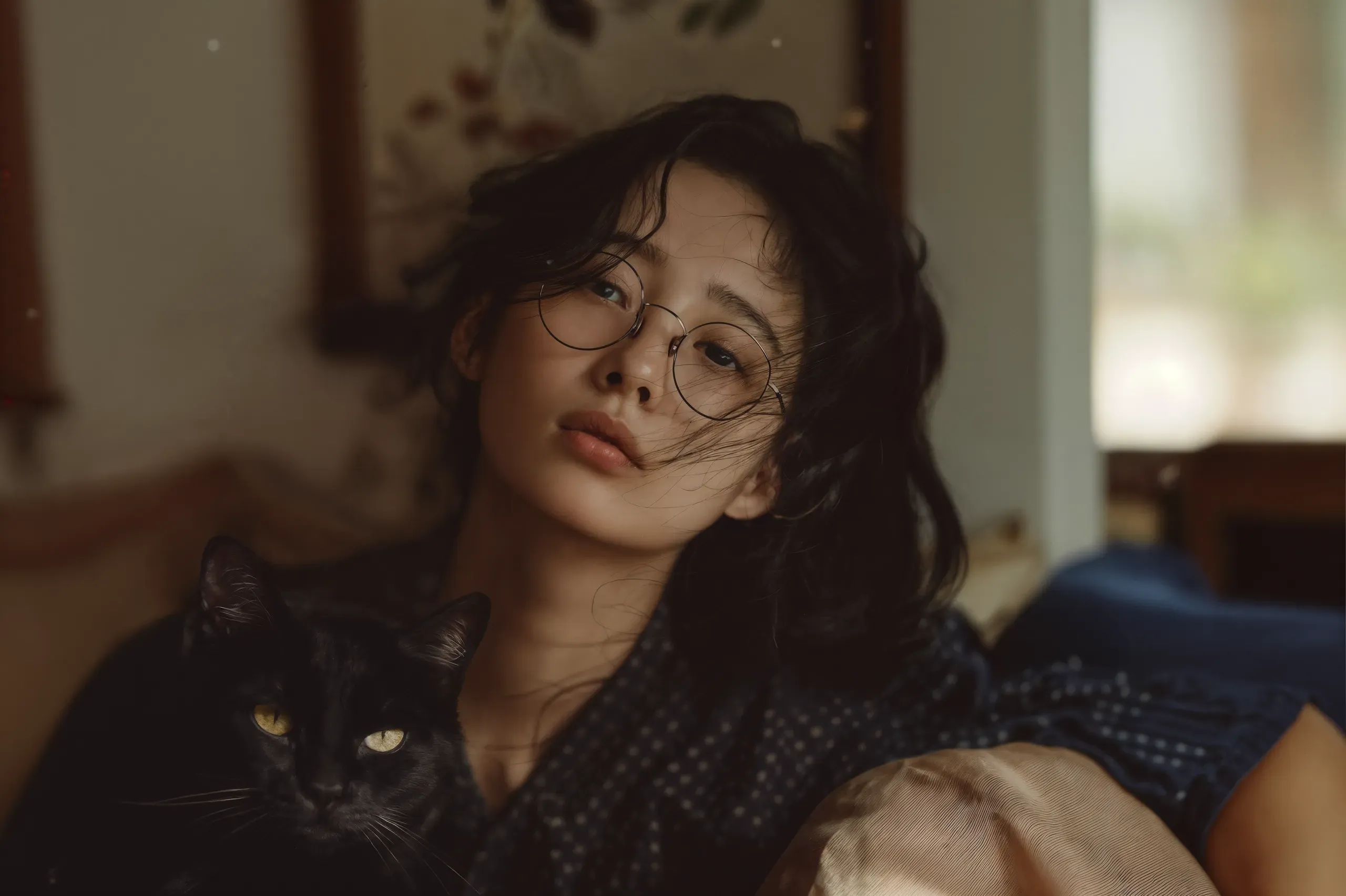 AI-generated portrait of a woman in round glasses leaning back in a dim, warm room with a black cat beside her