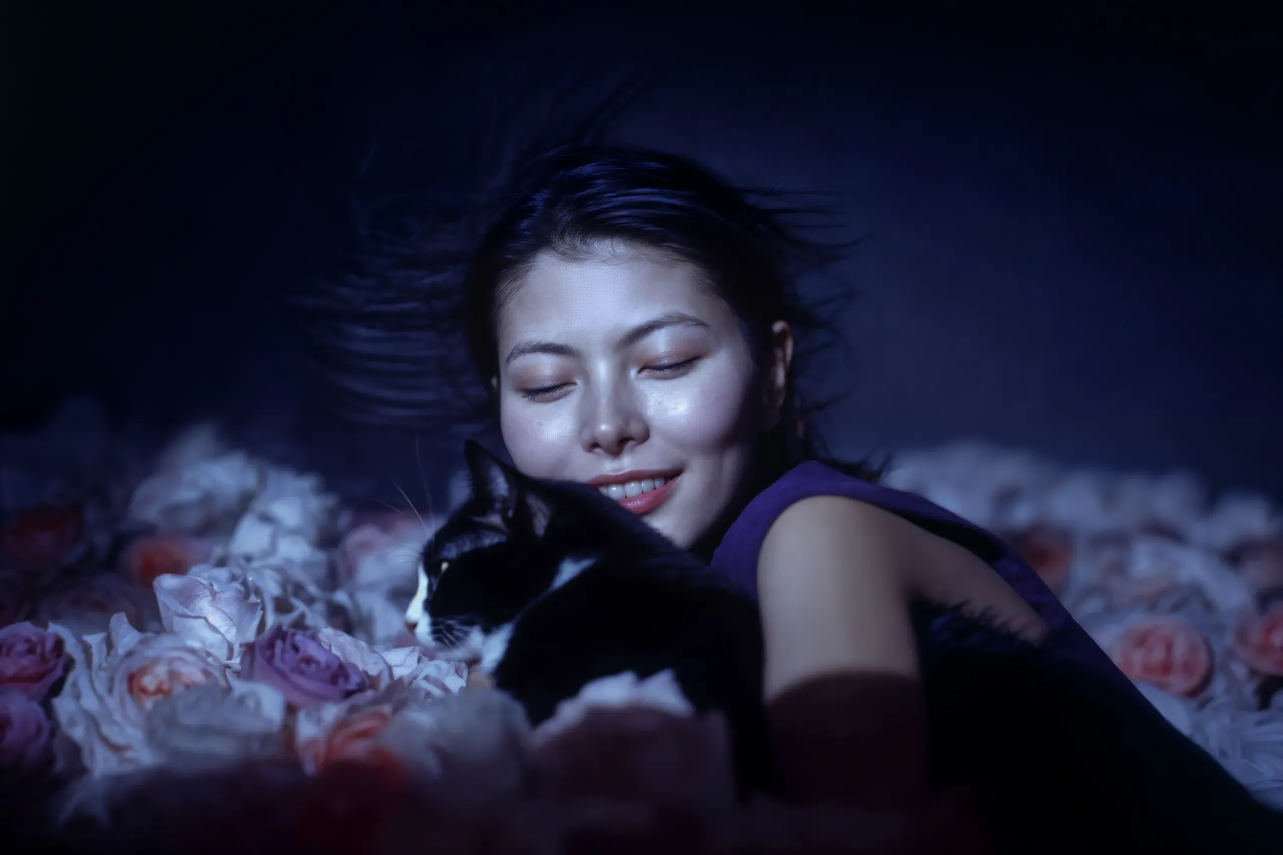 AI-generated portrait of a smiling woman with closed eyes hugging a black-and-white cat on a bed of pale roses