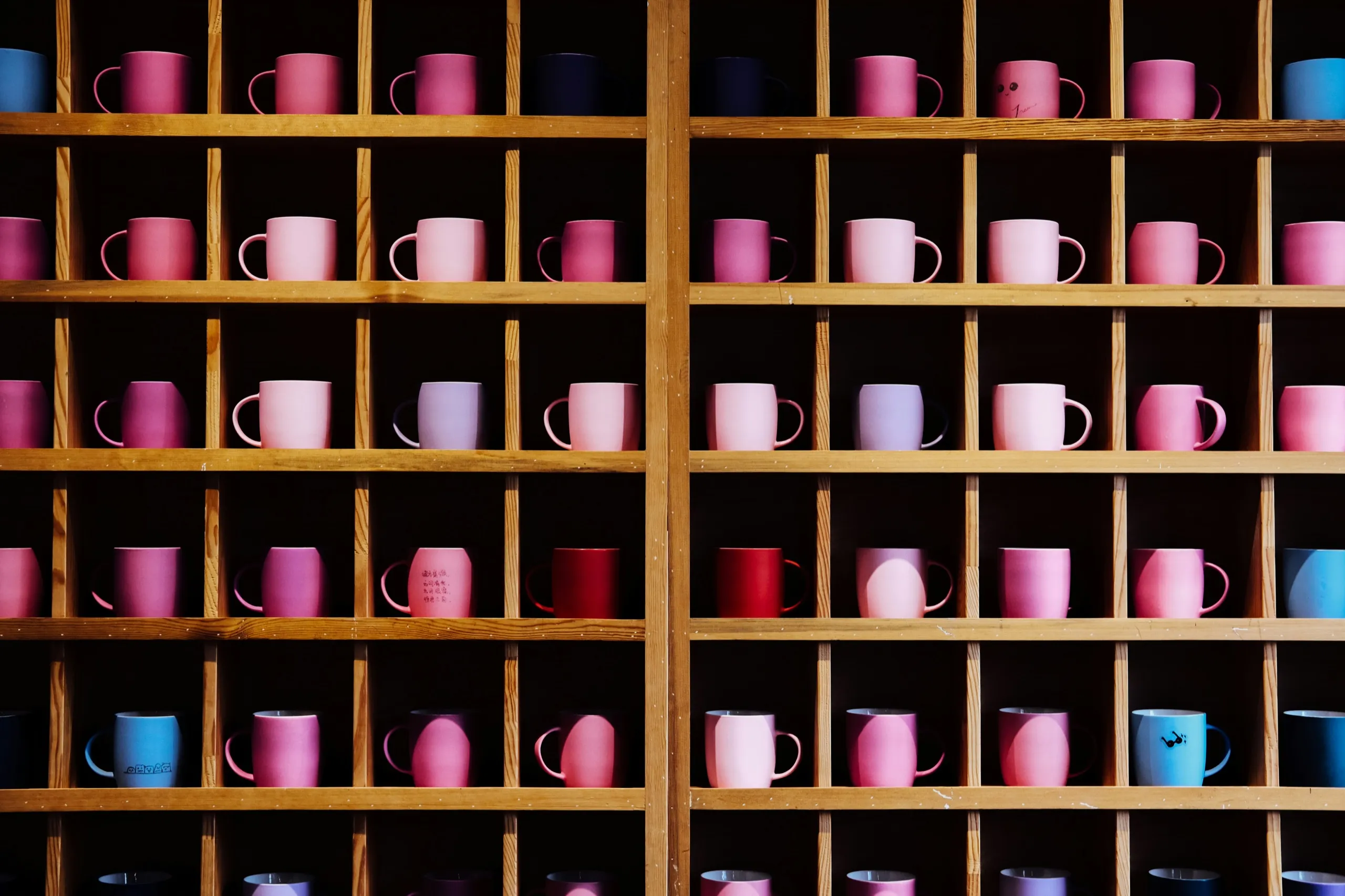 Pink and blue mugs arranged in the cubbies of a wooden shelf