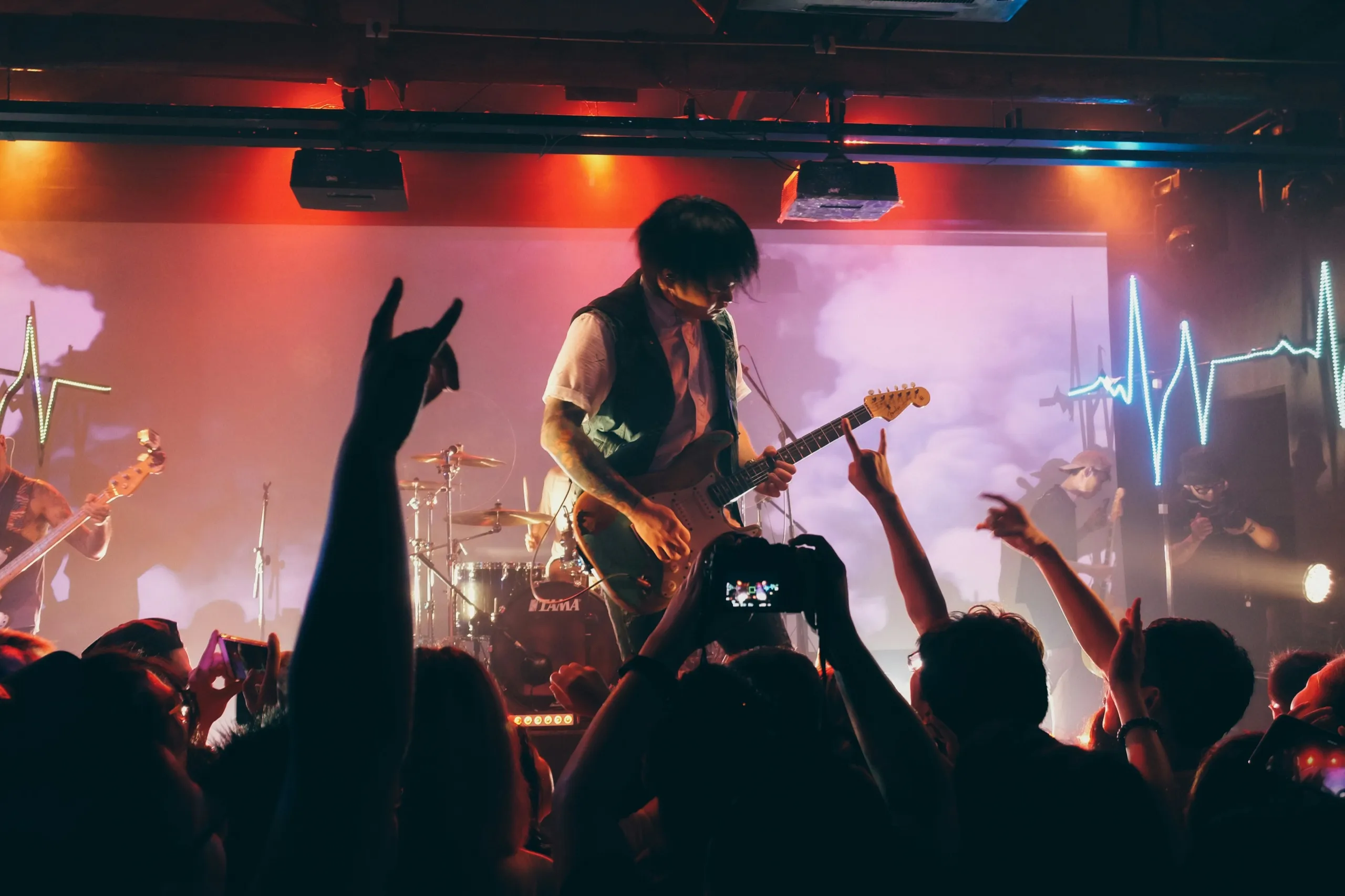 A guitarist in a club, the crowd’s raised hands in front of him